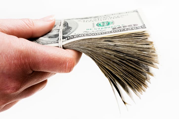 A man's hand holds out a large bundle of US dollars which could be payment, a bribe, or maybe wages. Isolated on white.