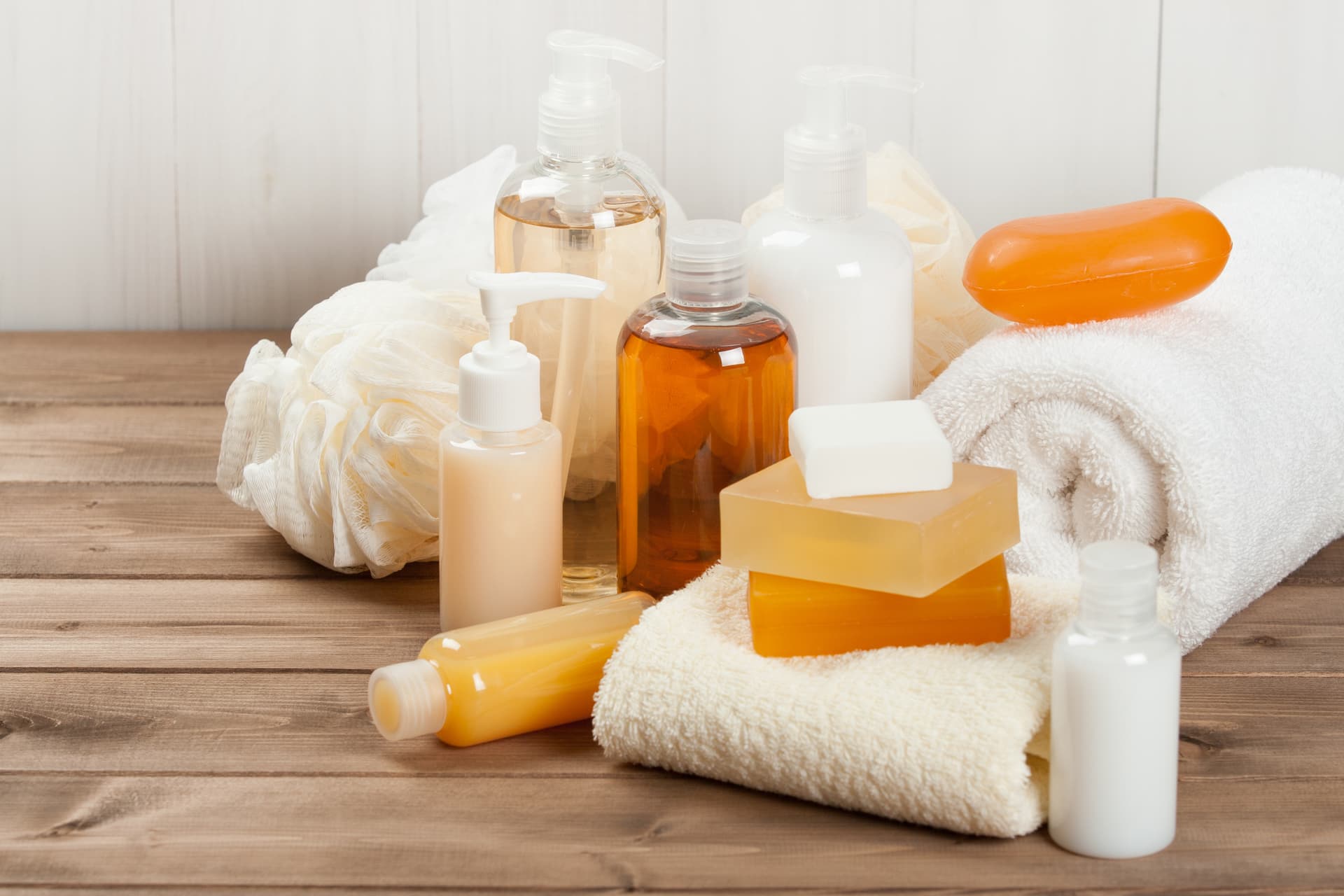 Image of personal care products, including a soap bar, shampoo, shower gel, loofas, and towels.