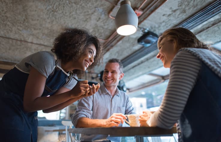 Happy waitress taking an order at a restaurant and talking to customers