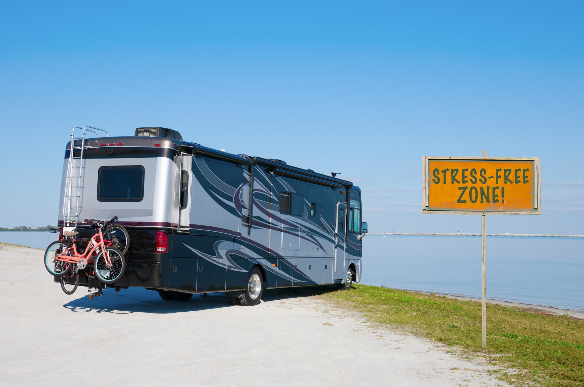 RV recreational vehicle at edge of water at a beautiful beach with a TRESS FREE ZONE! sign in the foreground.