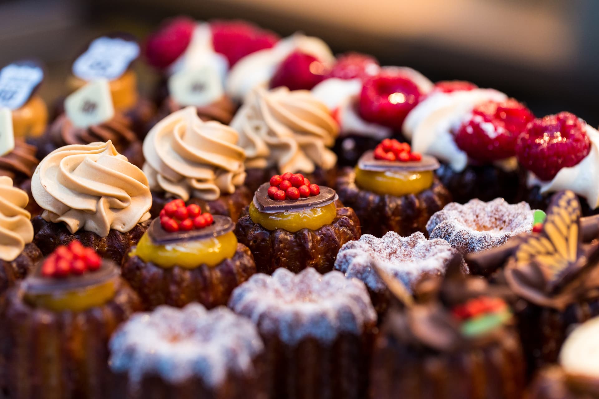Close up horizontal color image depicting a selection of freshly baked delicious cakes and cupcakes for sale at Borough Market in London, one of the oldest and most popular food markets in the world. The gourmet cakes are topped with all kinds of things, including whipped cream and fresh strawberries.
