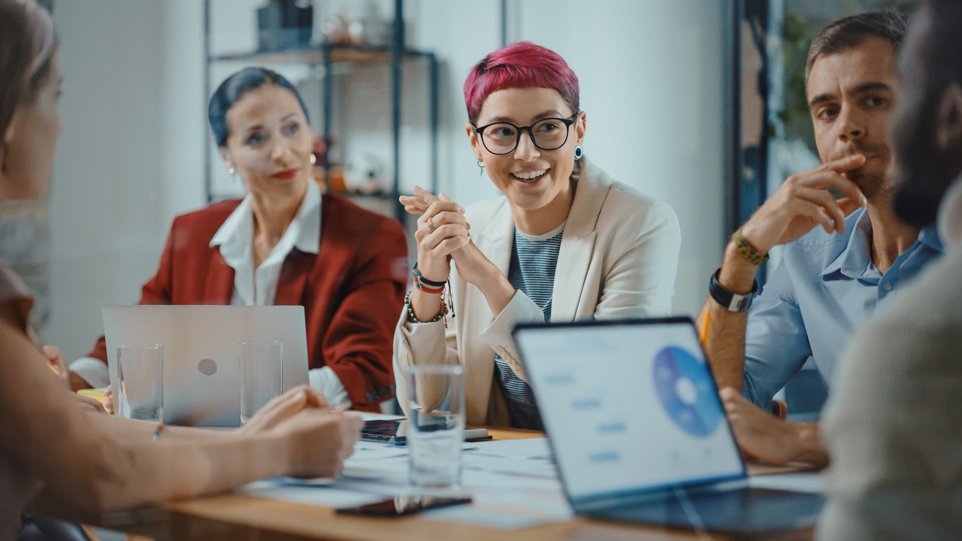 Group of diverse workers collaborate around a table looking at graphs on a laptop