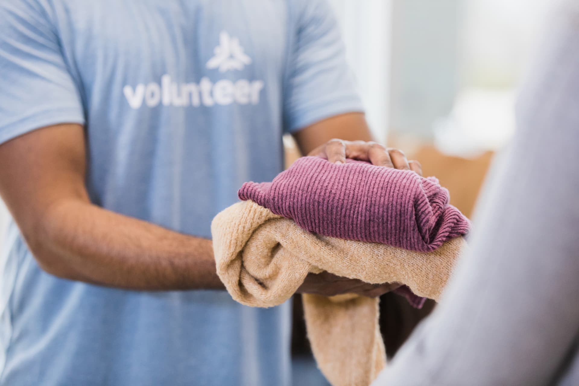 The unrecognizeable person hands some folded clothing items to another person.