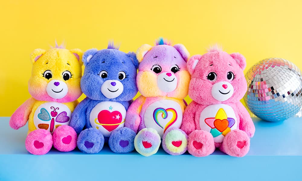 multi-colored Care Bear stuffed animals sitting in front of yellow background