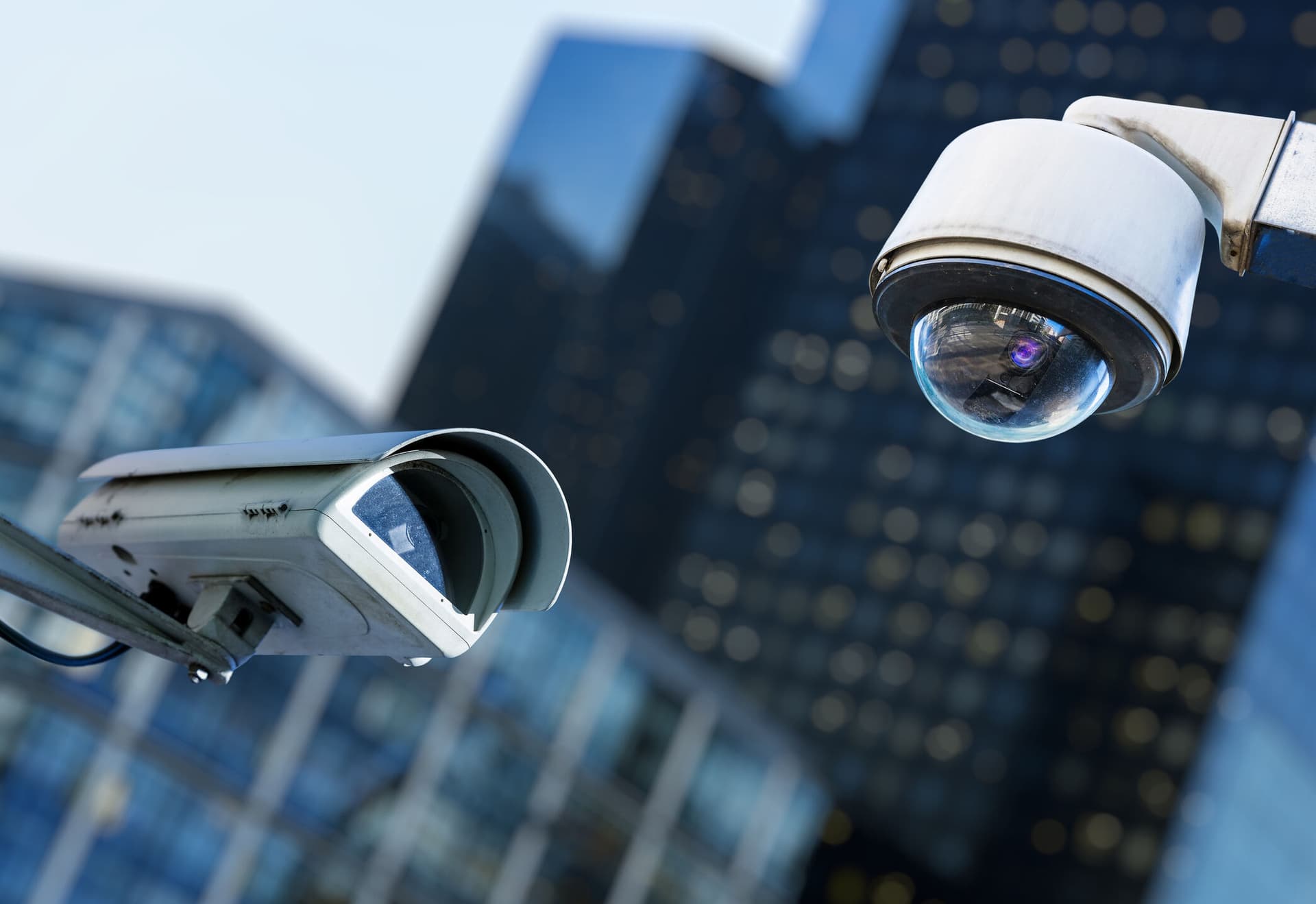 two cctv security camera in a city with blurry business building on background
