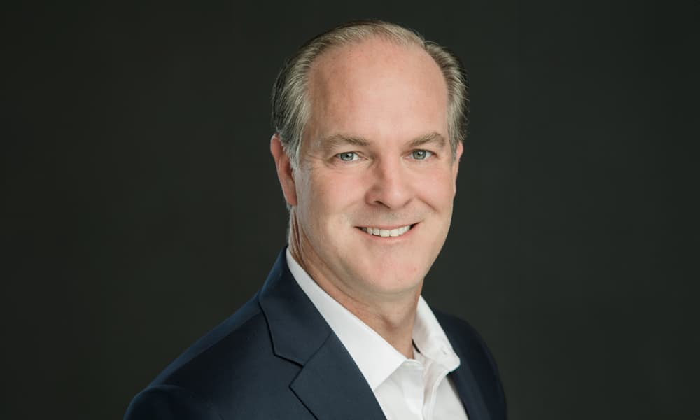 Headshot of Alex Darden in dark blazer and white shirt against dark background.