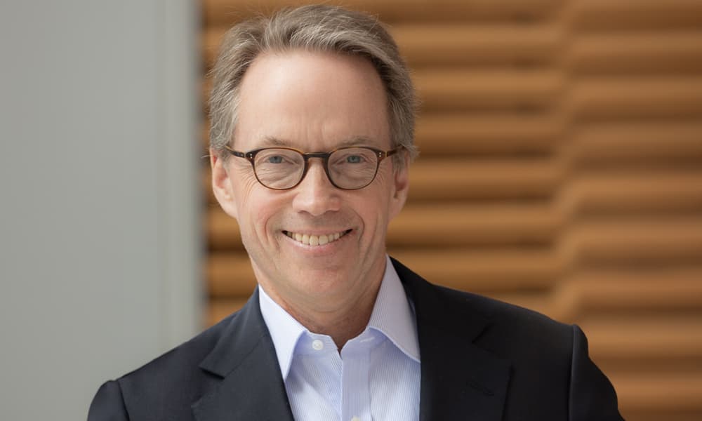 Headshot of Hamilton Lane wearing black blazer, light shirt and glasses against paneled background