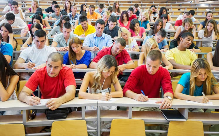 "Group of college students in the university amphitheatre, they are sitting and doing an exam."