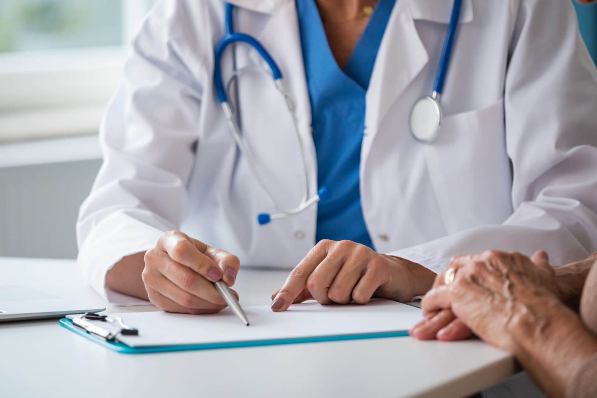 Midsection of female doctor sitting at the desk in an office and discussing test results with senior woman. Close up of hands, unrecognizable people.