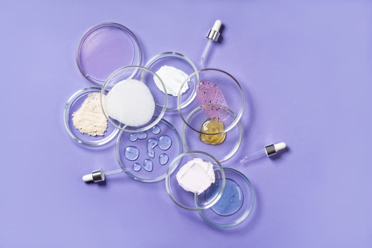 Cosmetic products, scrub, face serum and gel in many petri dishes on a pink background. Cosmetics laboratory research concept.