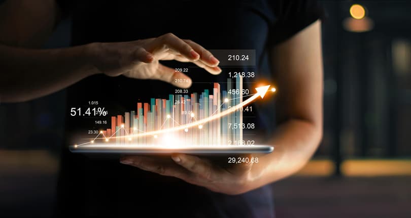 Businessman holding tablet and showing a growing virtual hologram of statistics, graph and chart with arrow up on dark background. Stock market. Business growth, planing and strategy concept