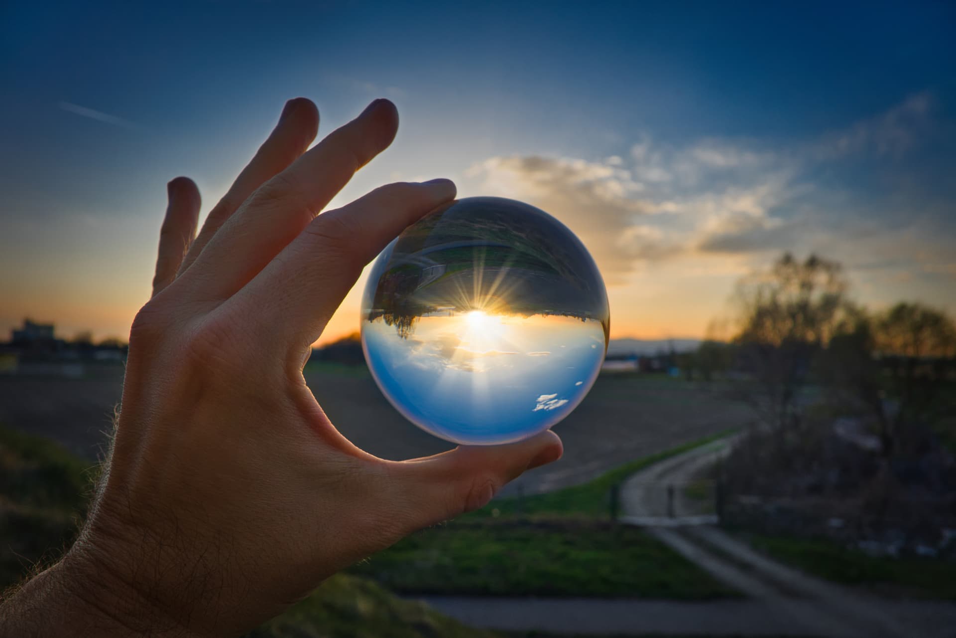 hand holding a crystal ball against the sun setting. The ball reverses the image