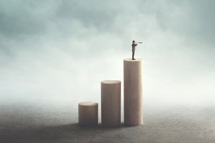 A man with a telescope standing at the top of a bar chart, looking out at cloudy skies