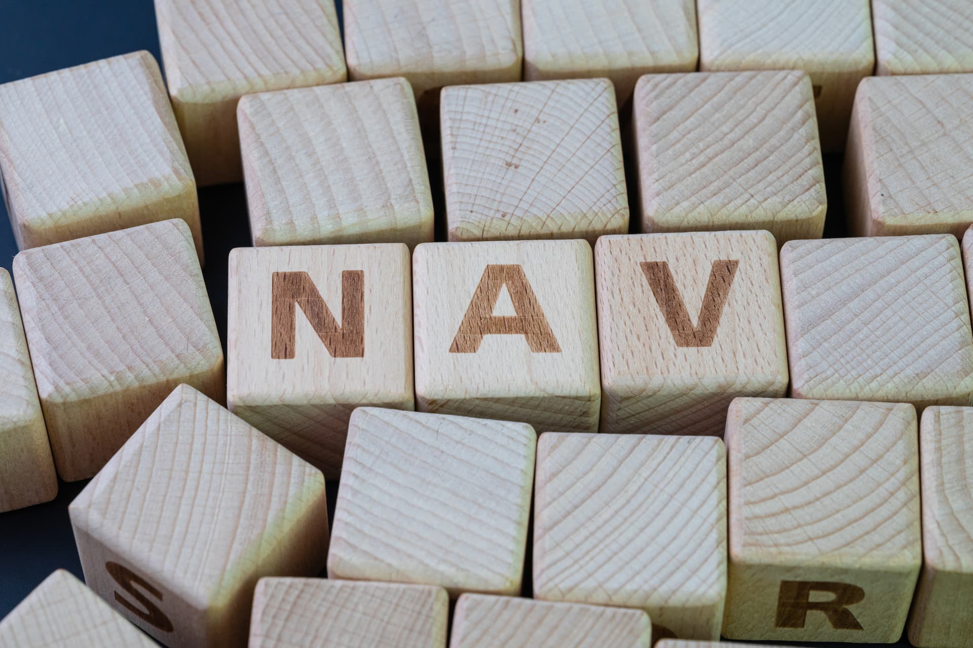 Net asset value (NAV) value of an entity's assets minus the value of its liabilities concept, cube wooden block with alphabet combine the word NAV on black chalkboard background
