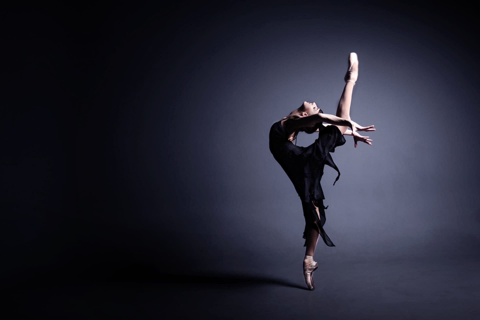 Young ballerina in a black suit is dancing in a dark studio