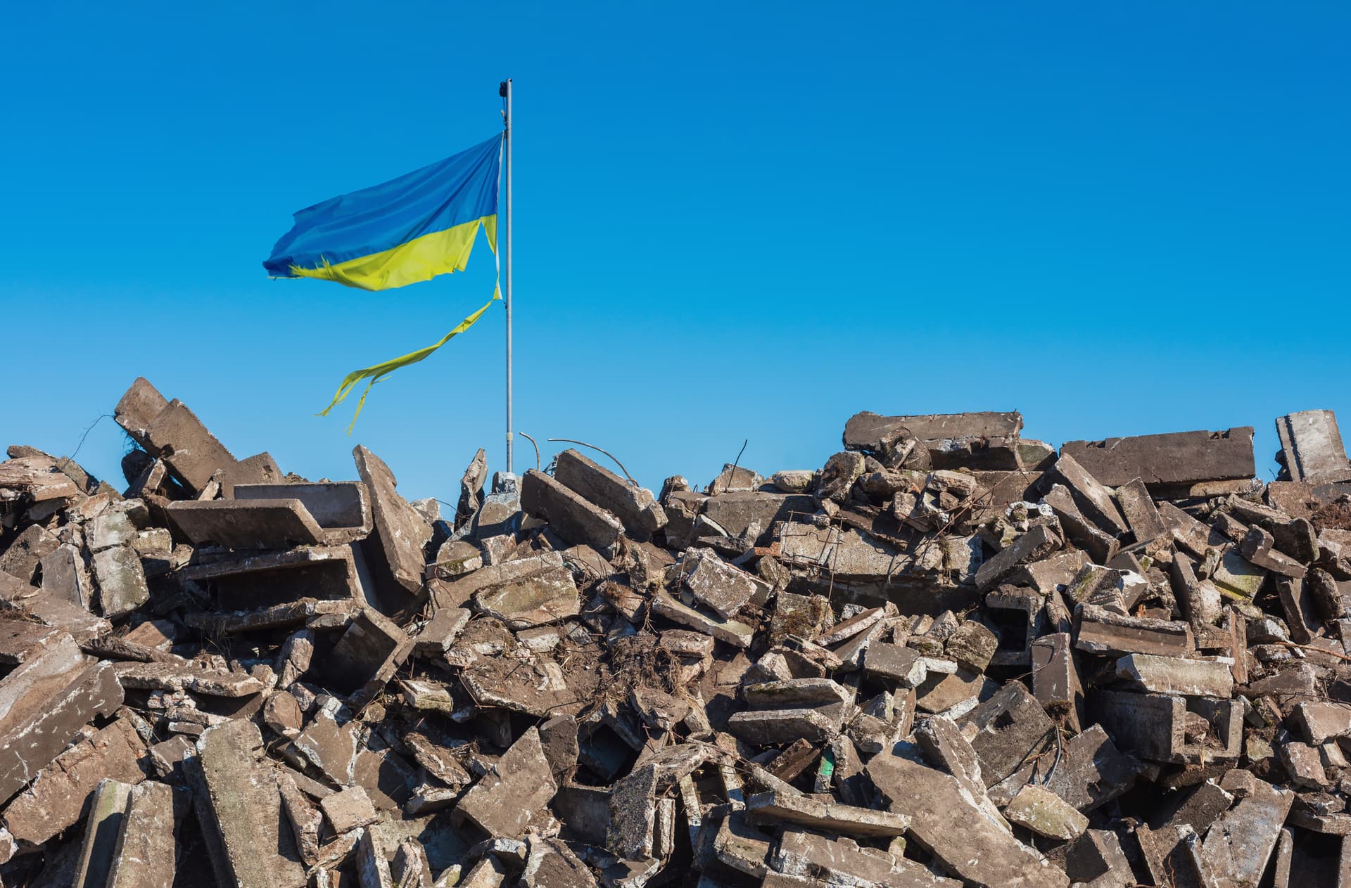 Damaged Ukranian flag flies over a destroyed builkd