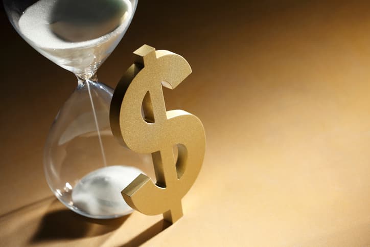 A dollar sign leaning against an hourglass