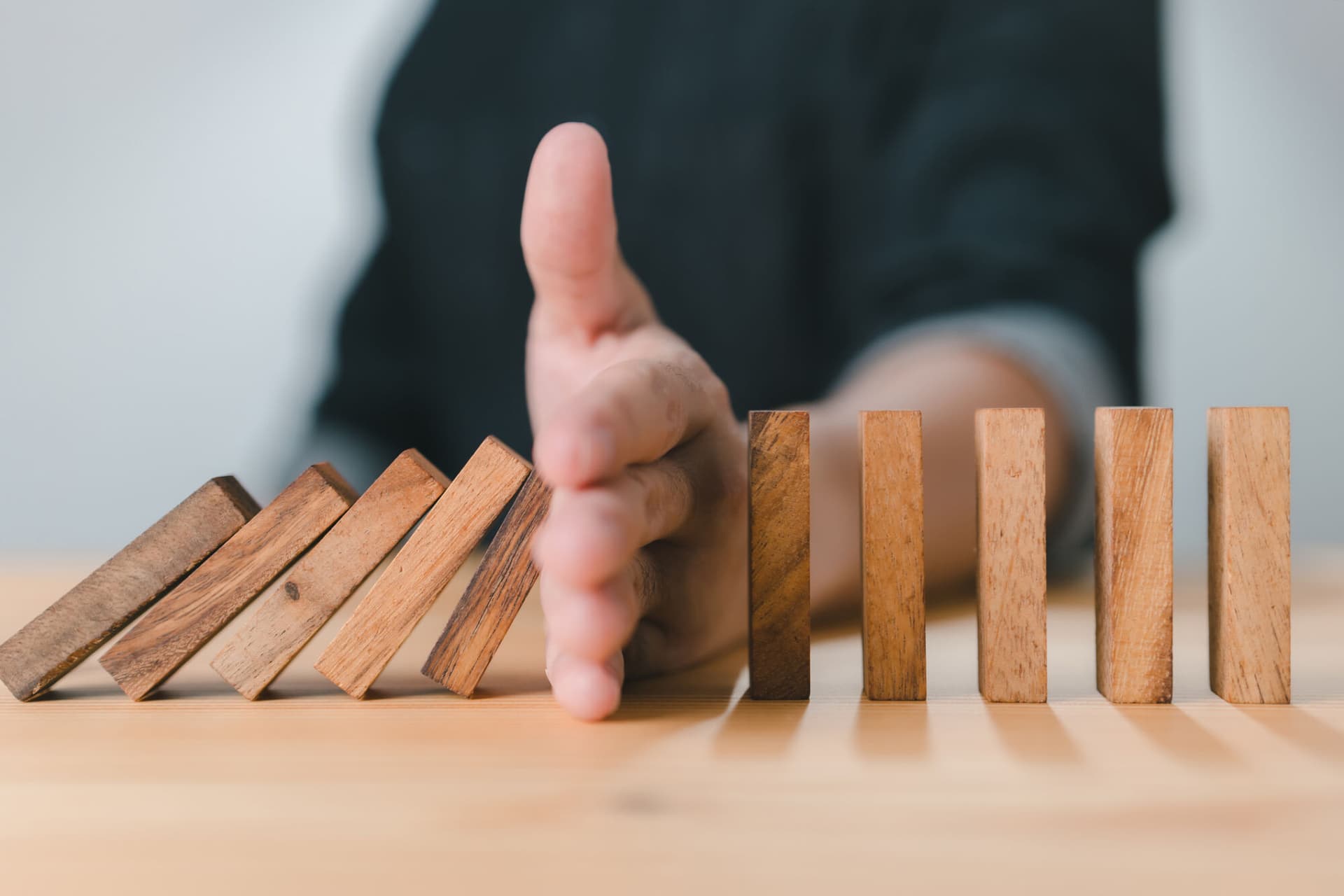 A businessman placing his hand between a series of wooden dominos blocks, stopping them all from falling