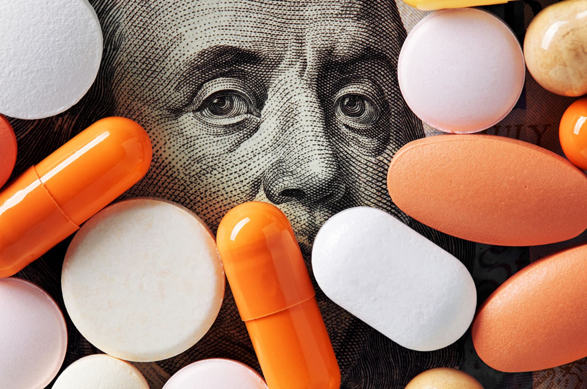 Money and healthcare policy concept. Colorful medical pills cover Benjamin Franklin's face on one hundred american dollar bill. Macro top down view.