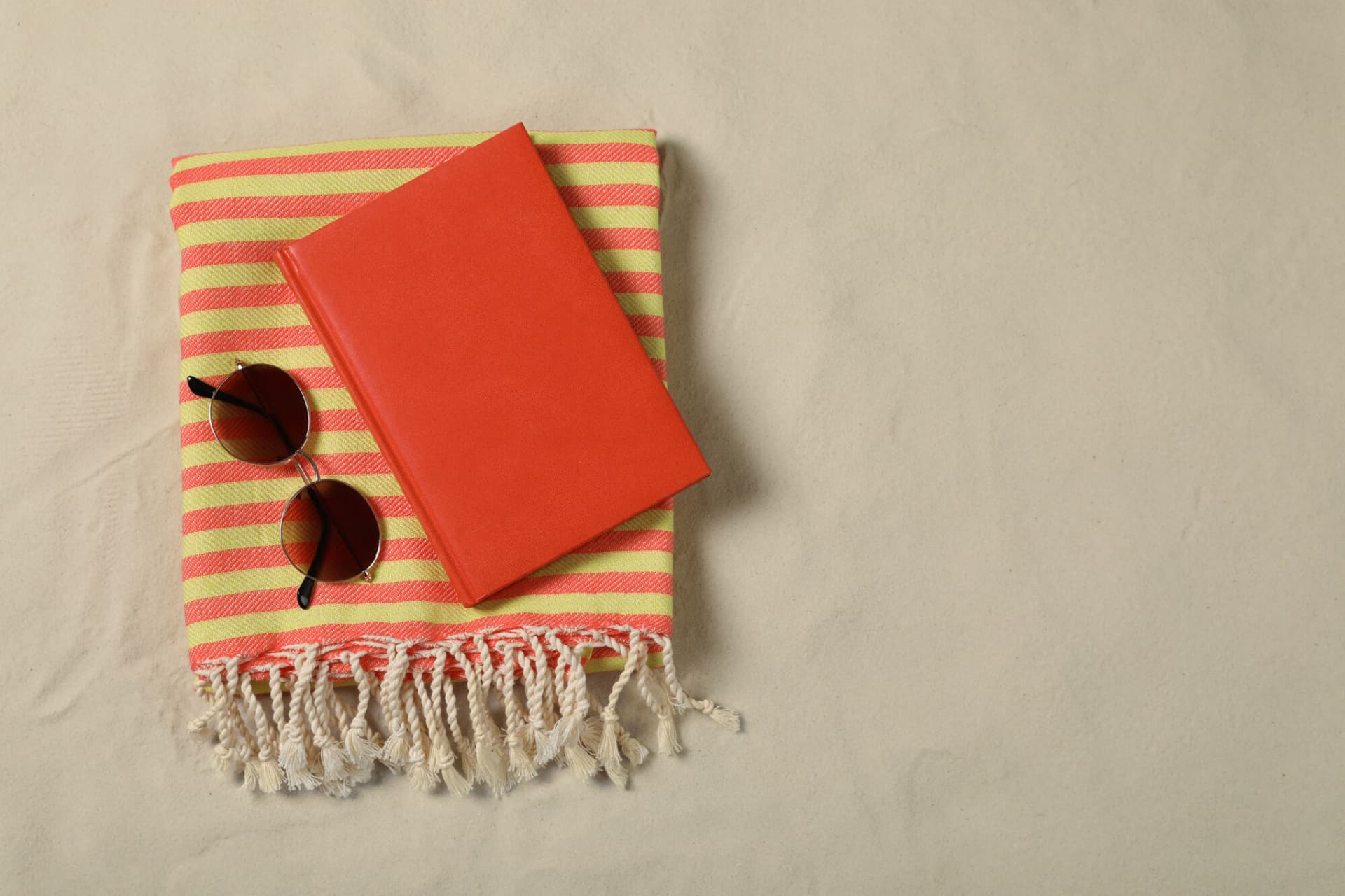 A book and a pair of sunglasses on a striped towel at the beach