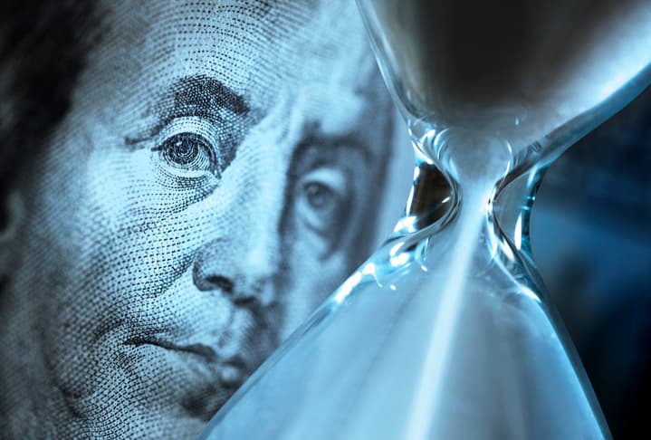 A US bank note set behind an hourglass