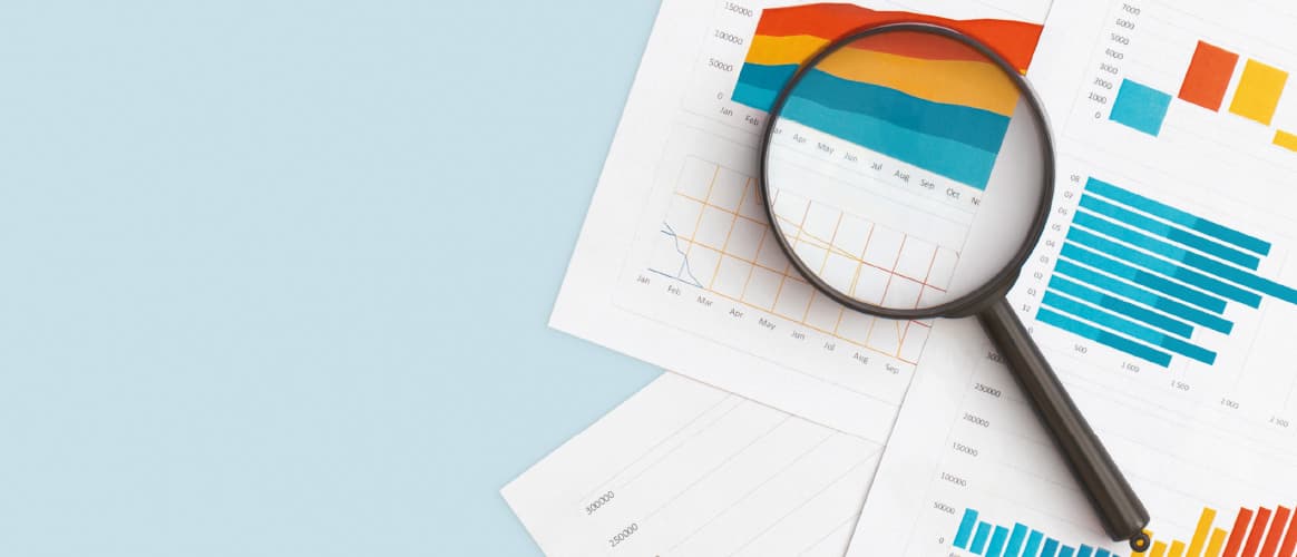 A magnifying glass lies on top of several documents of infographics