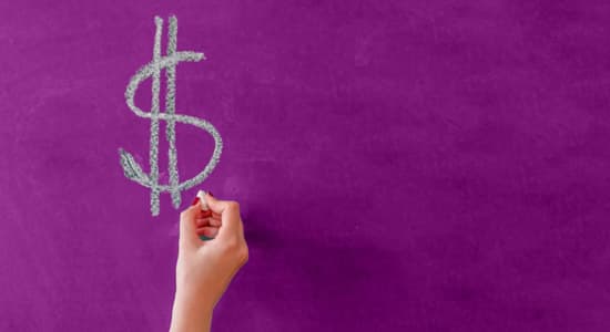 A hand writing a USD sign on a chalkboard